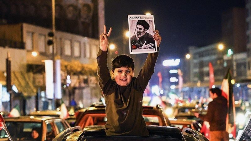 Boy holds up victory sign and poster of Iranian supreme leader