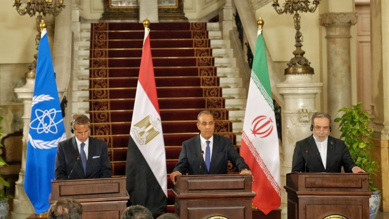 three men at podiums in front of the Iranian, Egyptian, and IAEA flags, respectively.