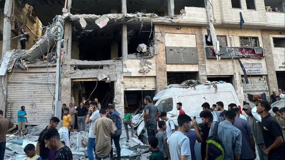crowd looks at a building with rooms blown out by airstrike