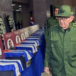 Raúl Castro walks in front of coffins with Cuban flags over them