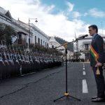 Rodrigo Paz stands in front of microphone in front of row of soldiers with muskets